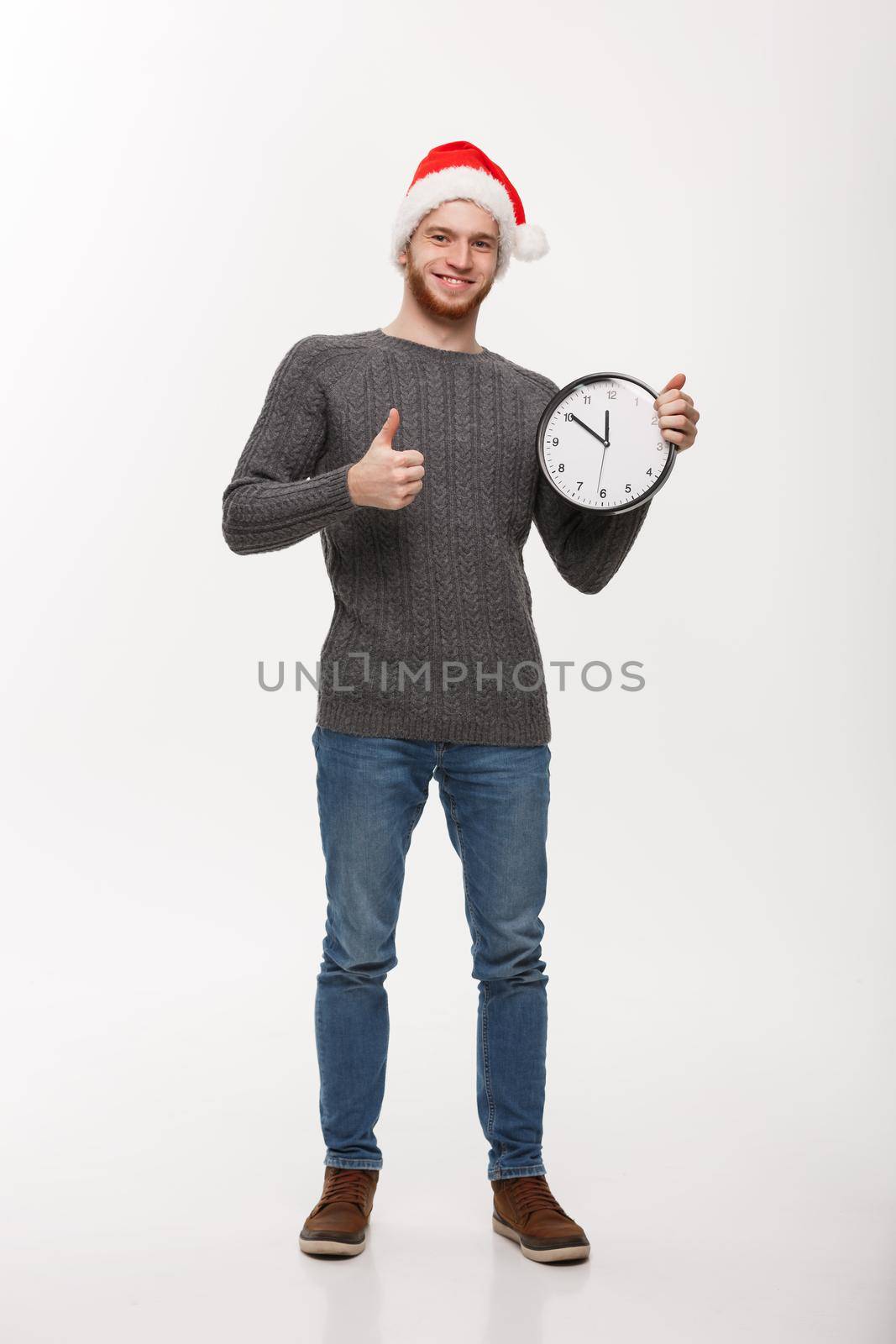 Holiday concept - Young handsome beard man thumb up on white clock.
