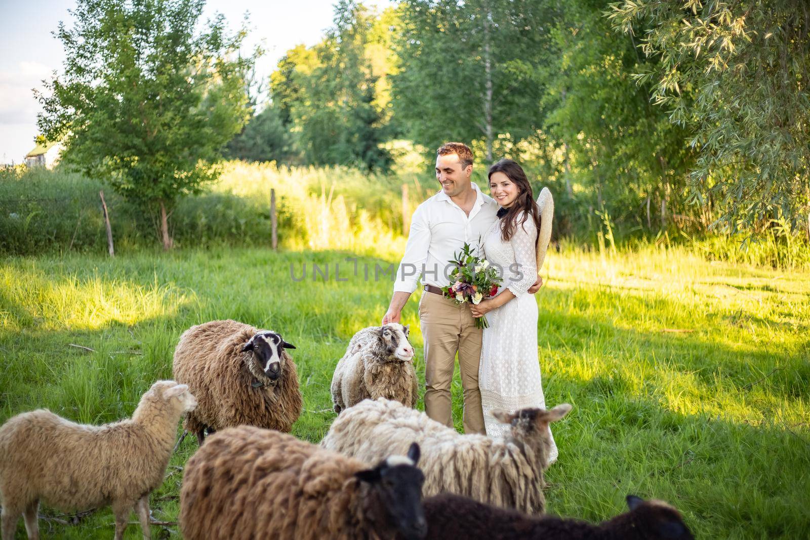 Bride in a dress with a bouquet puts a hat on and laughs. Rustic wedding in the style of boho at the ranch. by Anyatachka