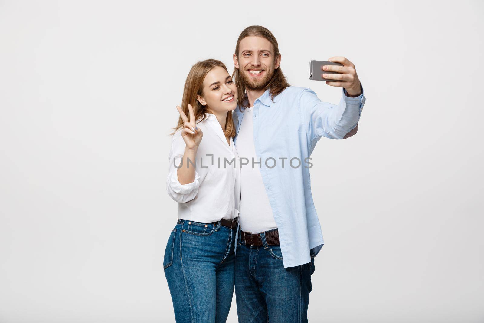 Portrait of a happy couple making selfie photo with smartphone over isolated white studio background. by Benzoix