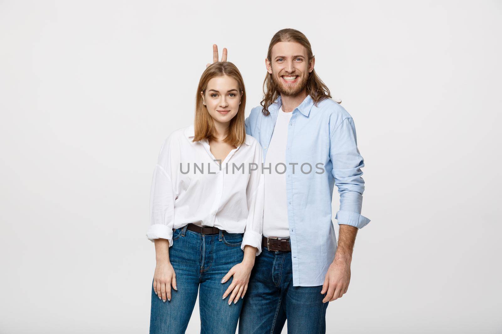 Portrait of lovely young couple showing peace or victory sign on white studio background.