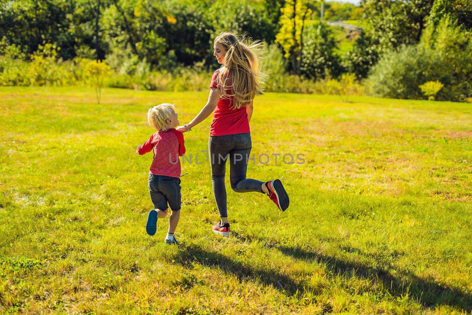 Mom and son run on the green grass. Happy family in the park by galitskaya