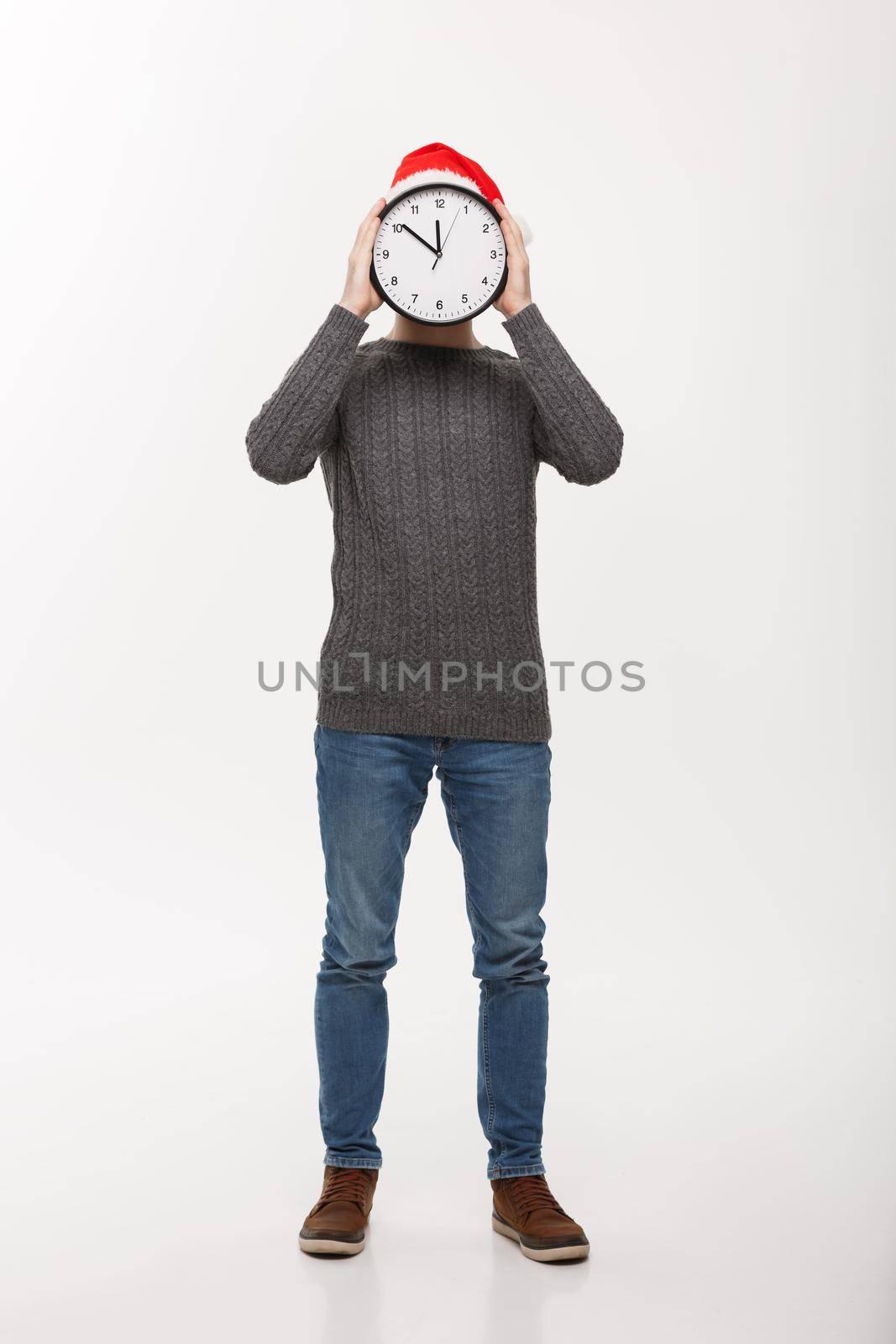 Holiday concept - Young handsome beard man hidden behind white clock over white studio background.