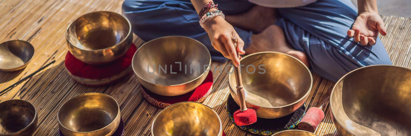 Woman playing on Tibetan singing bowl while sitting on yoga mat against a waterfall. Vintage tonned. Beautiful girl with mala beads meditating. BANNER, LONG FORMAT