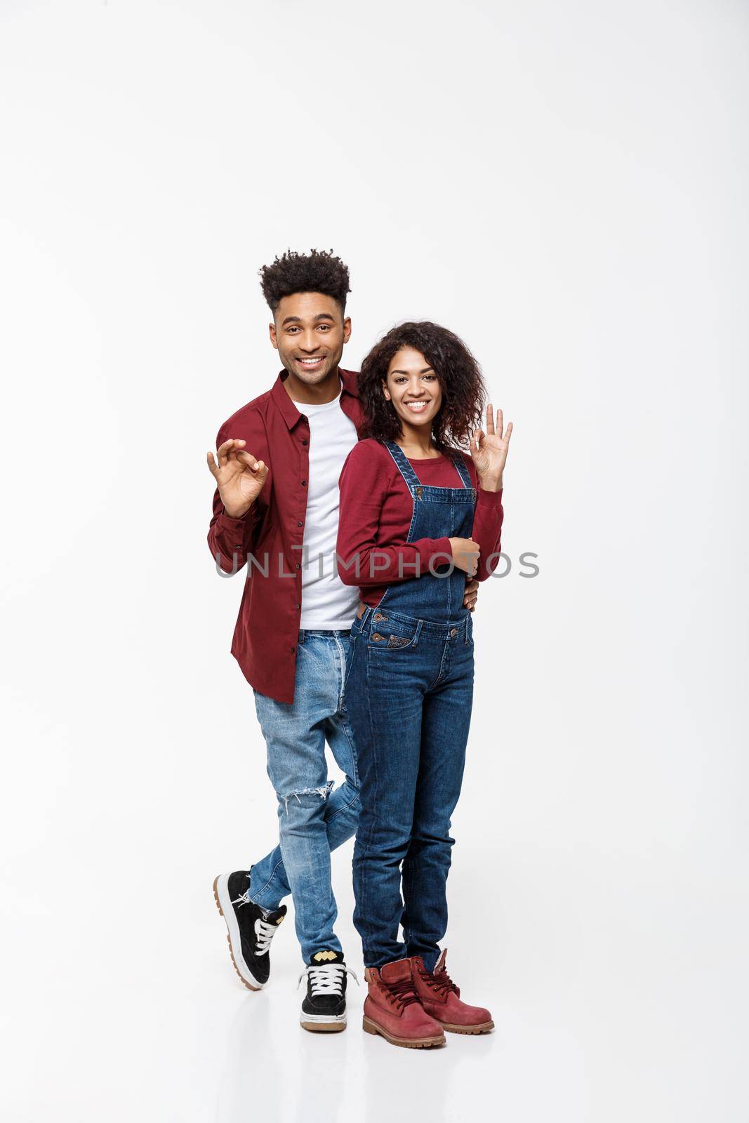 Lifestyle Concept - Full length portrait of a happy smiling african couple standing and showing ok gesture isolated over white background.