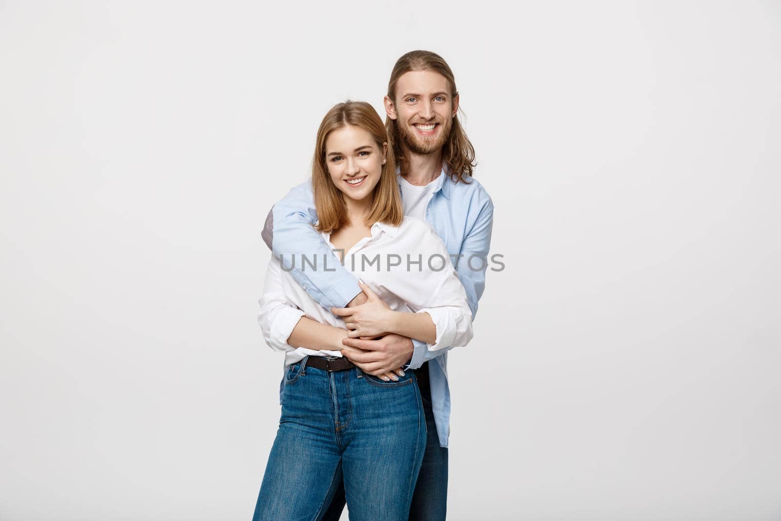 Portrait of cheerful young couple standing and hugging each other on isolated white background.