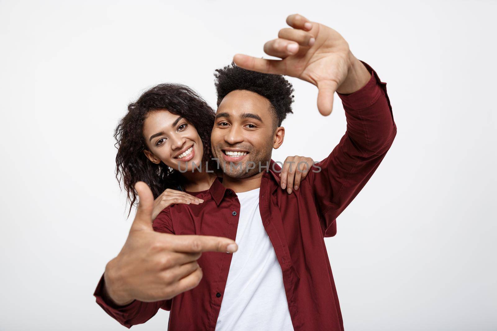 Happy young African American couple looking through a finger frame and smiling while standing isolated on white