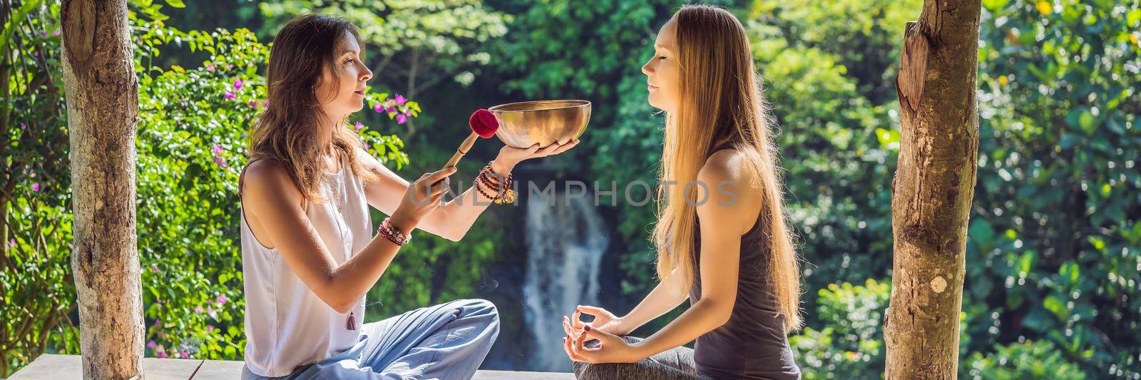 BANNER, LONG FORMAT Nepal Buddha copper singing bowl at spa salon. Young beautiful woman doing massage therapy singing bowls in the Spa against a waterfall. Sound therapy, recreation, meditation, healthy lifestyle and body care concept.