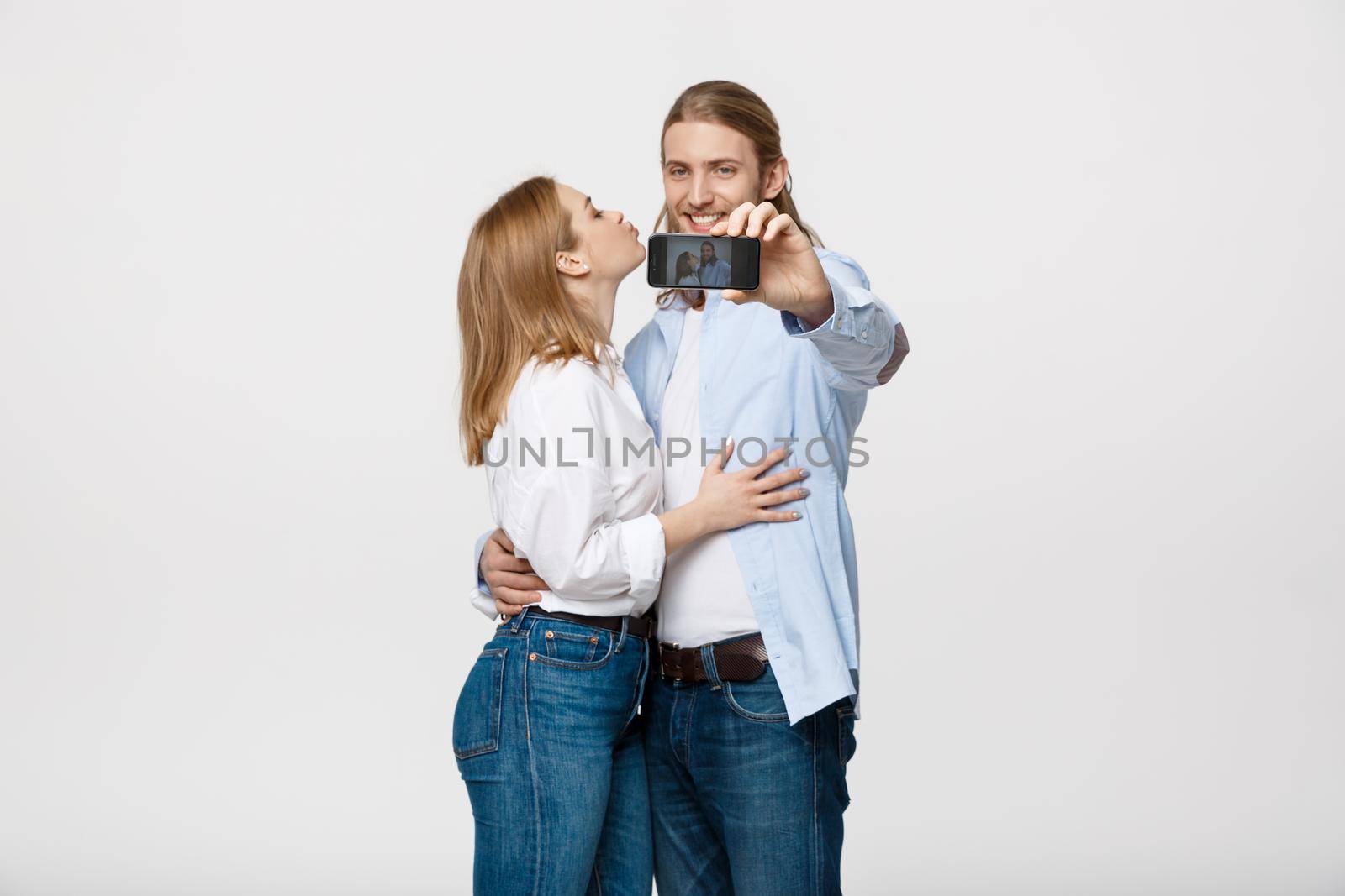 Portrait of a happy couple making selfie photo with smartphone over isolated white studio background