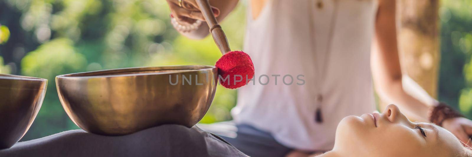 BANNER, LONG FORMAT Nepal Buddha copper singing bowl at spa salon. Young beautiful woman doing massage therapy singing bowls in the Spa against a waterfall. Sound therapy, recreation, meditation, healthy lifestyle and body care concept.