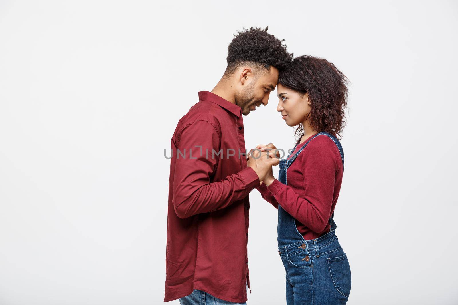 Side view of beautiful African American young couple in classic shirts holding hands, looking at each other and smiling. by Benzoix