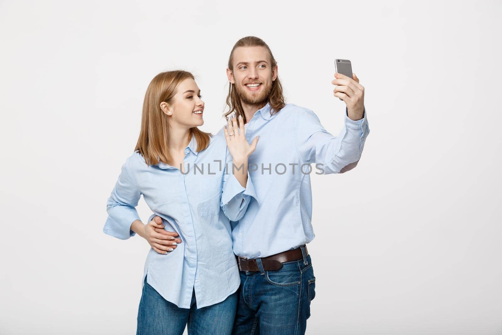 Joyful young loving couple making selfie on camera while standing in white studio background