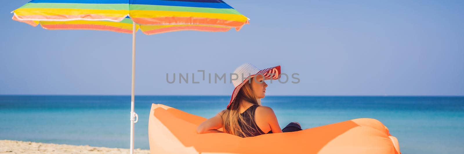 Summer lifestyle portrait of pretty girl sitting on the orange inflatable sofa on the beach of tropical island. Relaxing and enjoying life on air bed BANNER, LONG FORMAT by galitskaya