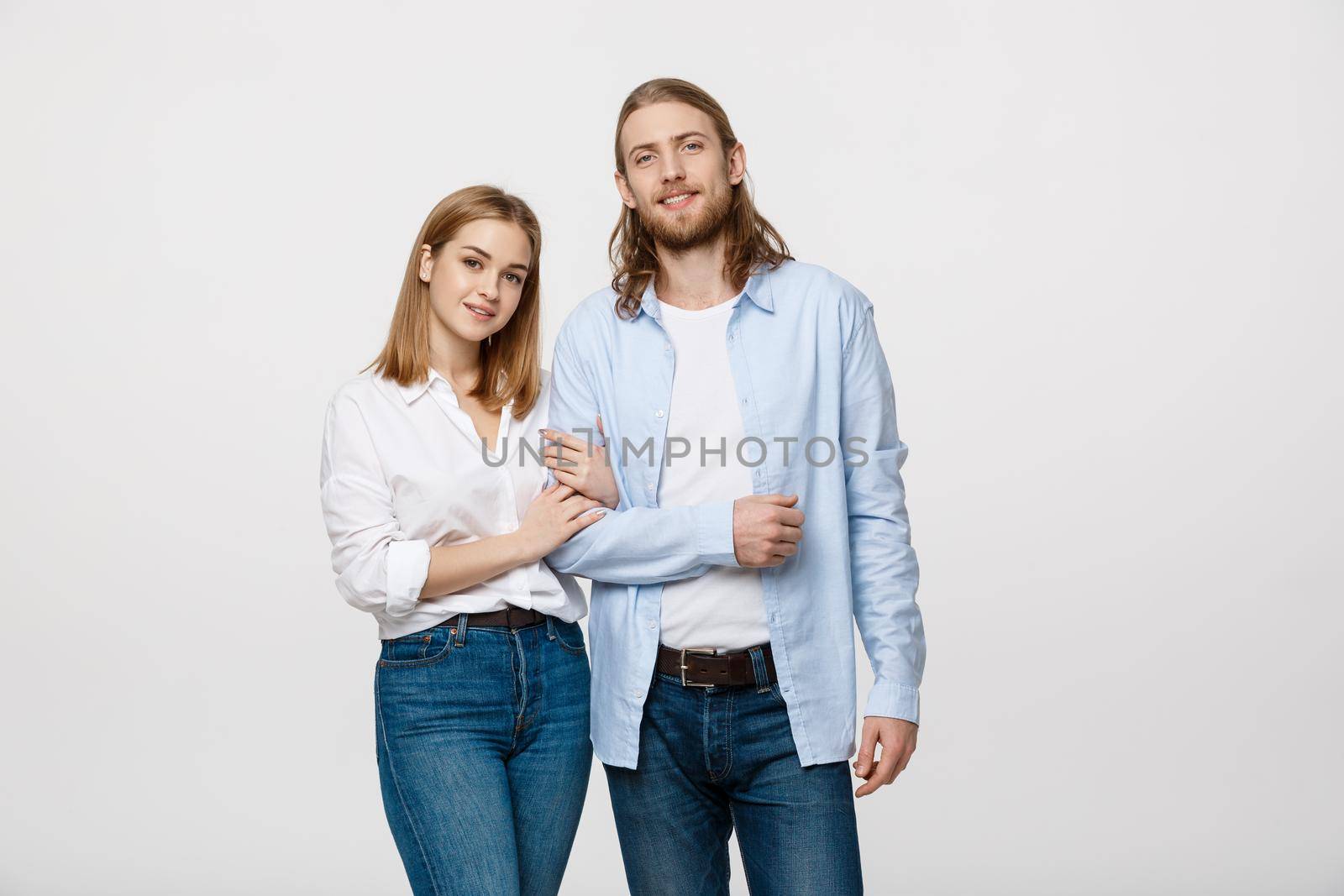Portrait of attractive young couple smiling for the camera while holding arm to arm. On grey background