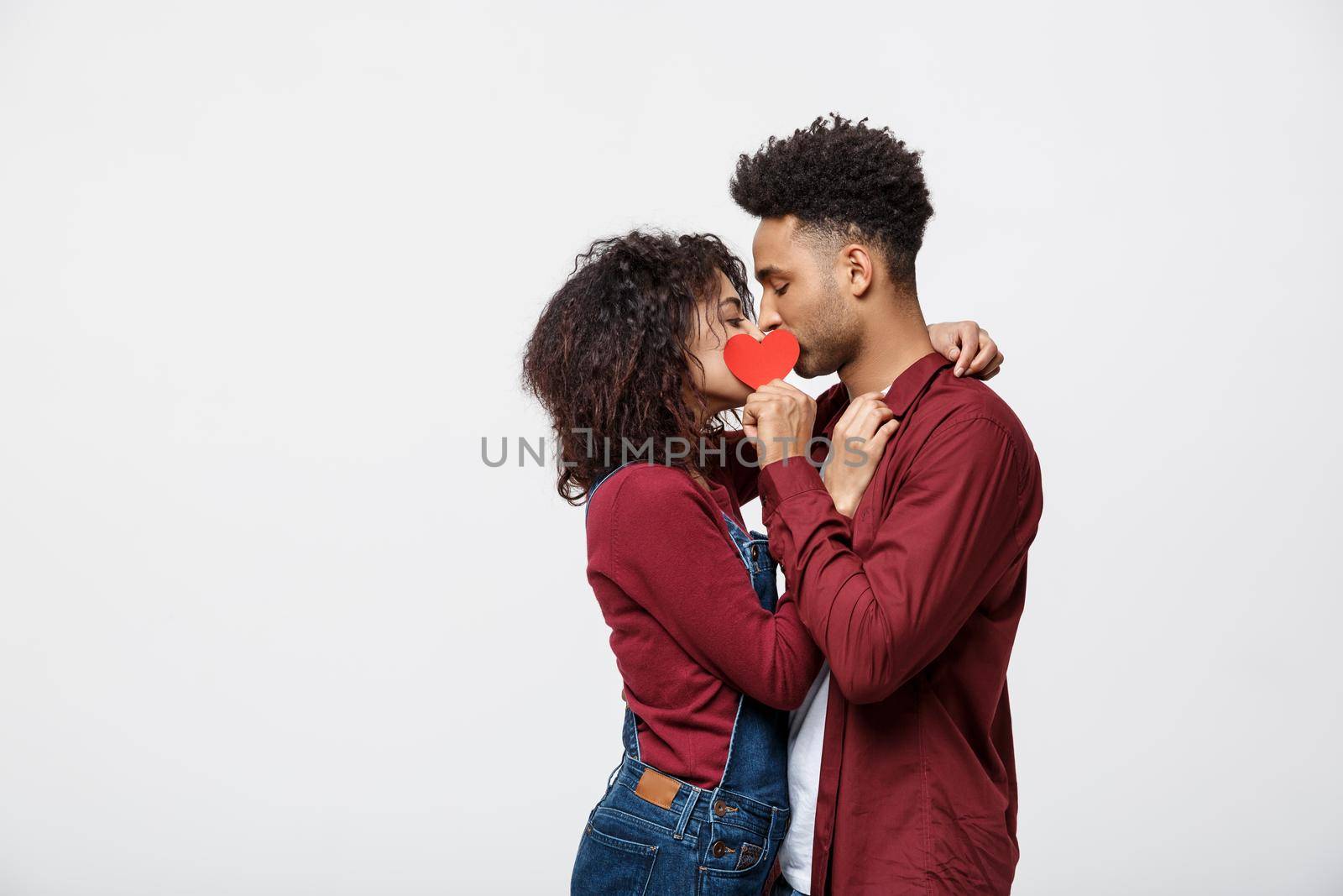 Two young attractive african american dates behind paper heart with their faces close to one another by Benzoix