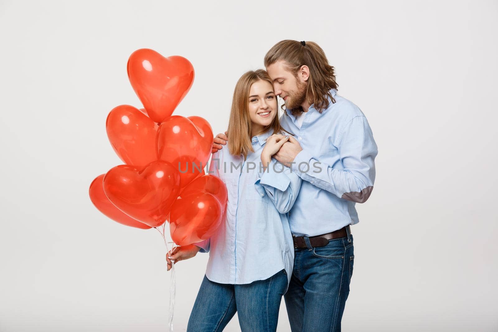 Portrait of young fashionable caucasian couple with balloons heart hugging at each other over isolated white background. by Benzoix
