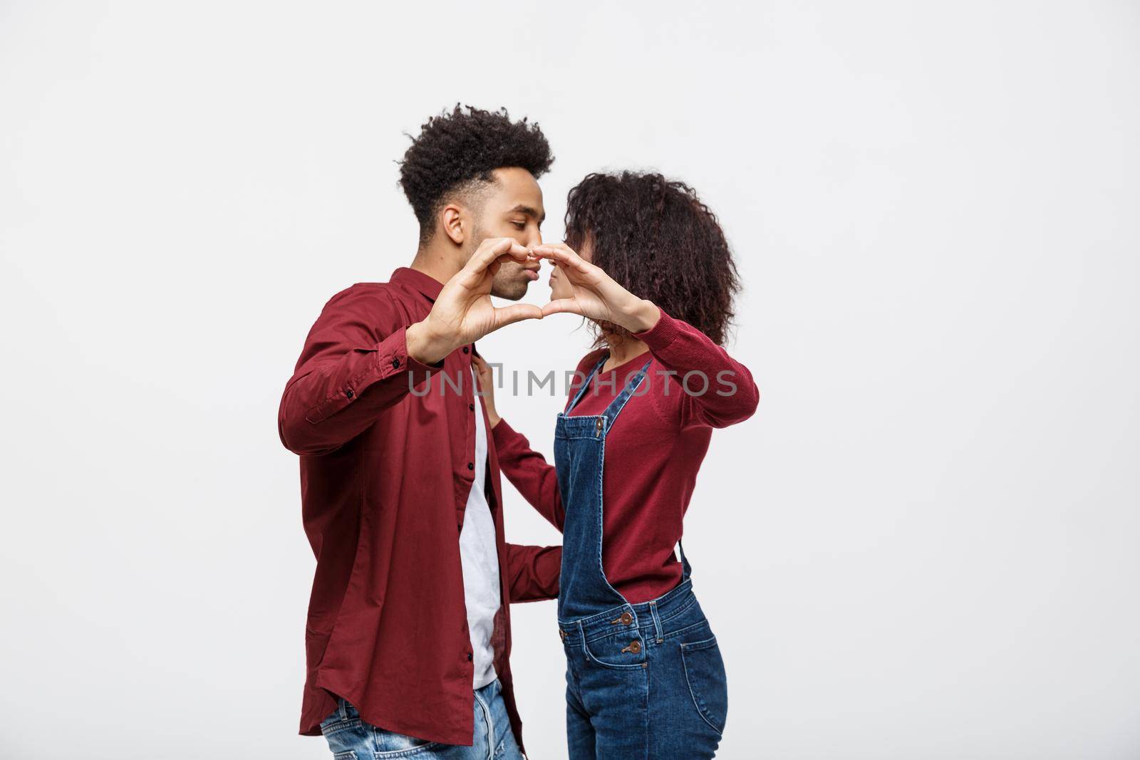 Portrait of a smiling young african couple dressed in casual clothes hugging and showing heart gesture with fingers isolated over white background.