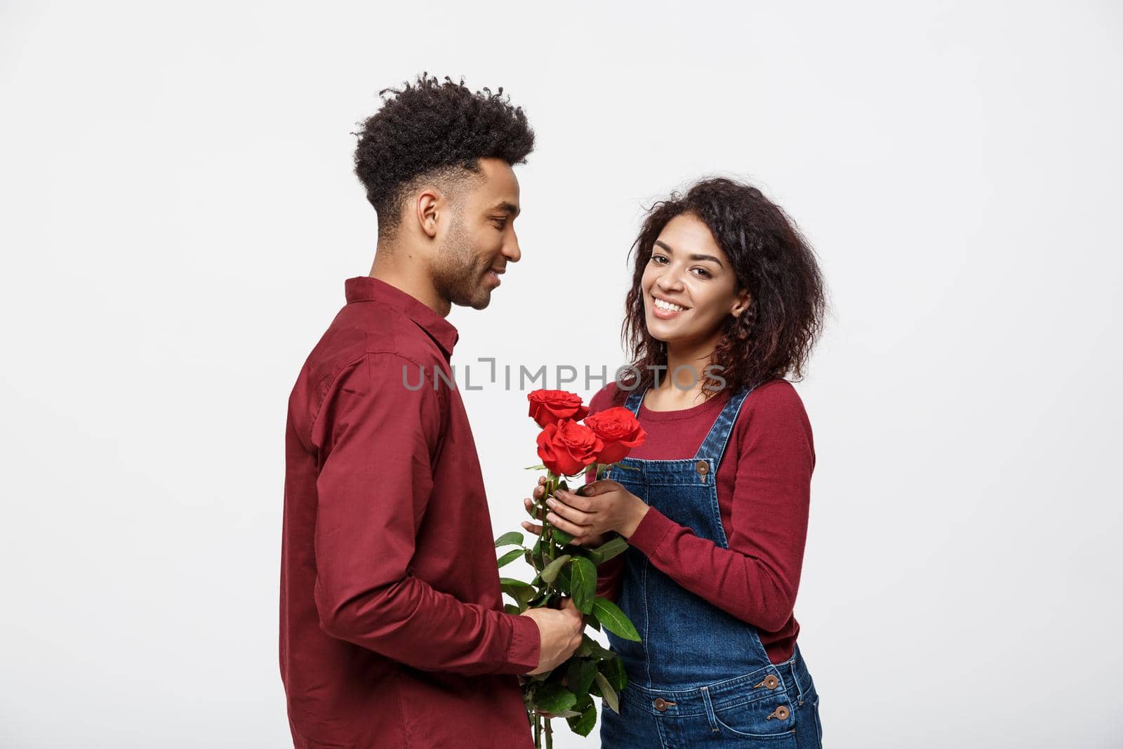 Beautiful elegant couple is hugging and smiling, on gray background. Girl is holding roses by Benzoix