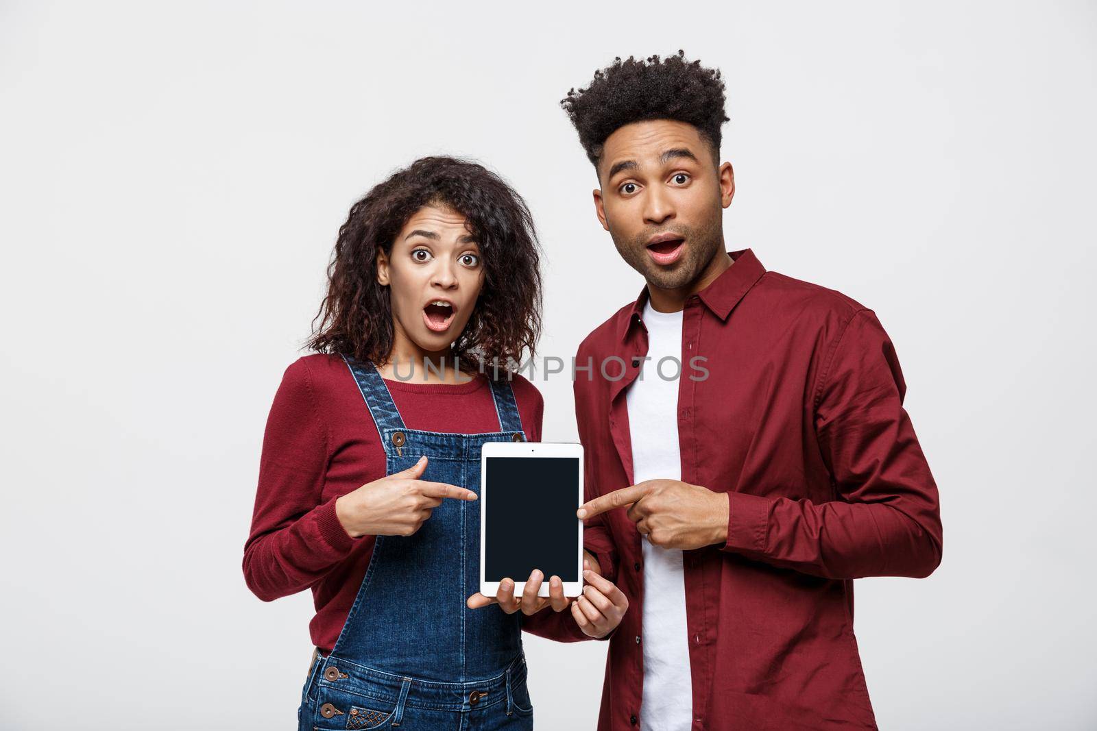 Portrait of African American couple holding table with shocking expression on white background.