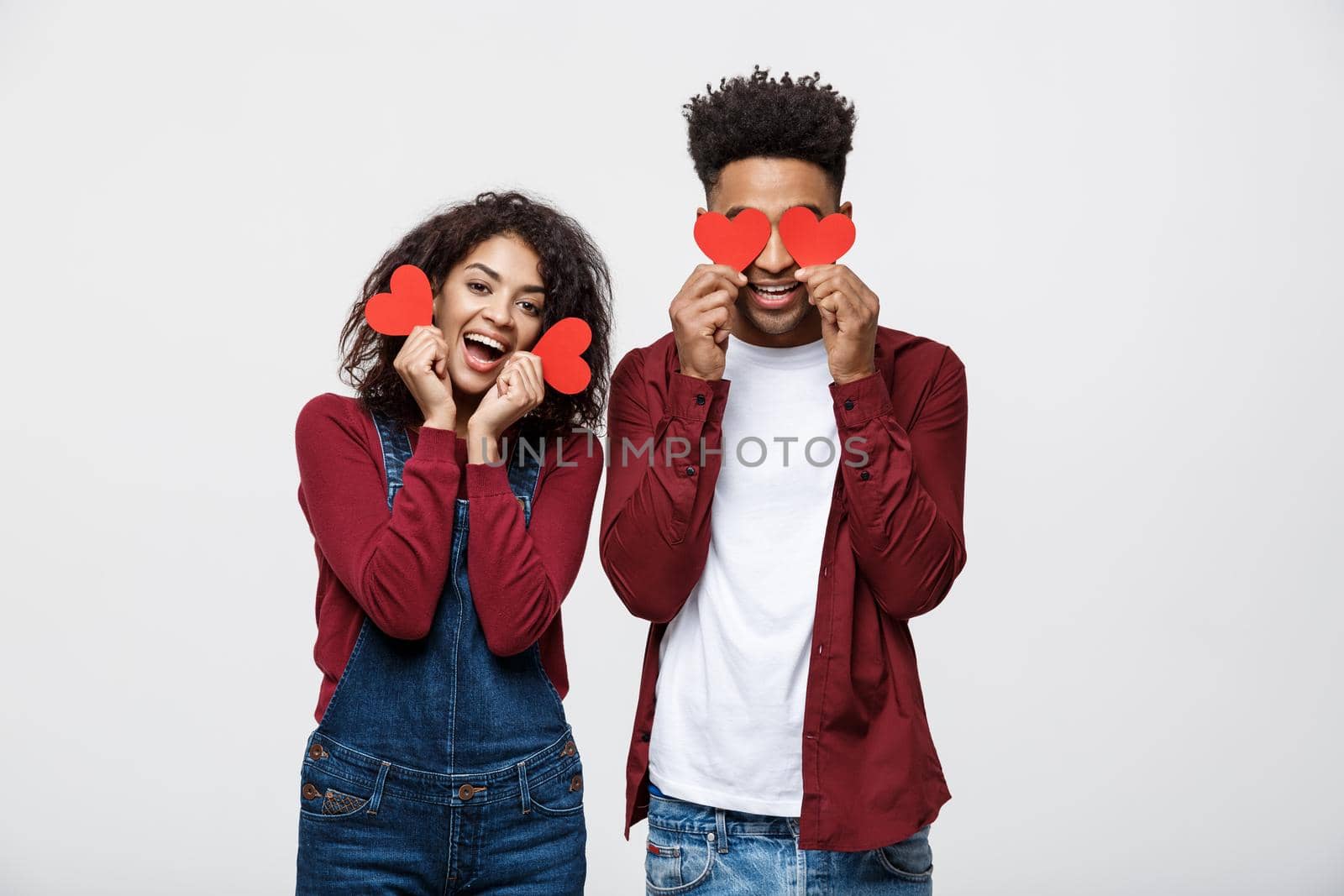 Beautiful Afro American couple holding two red paper heart, looking at camera and smiling, isolated on white background.