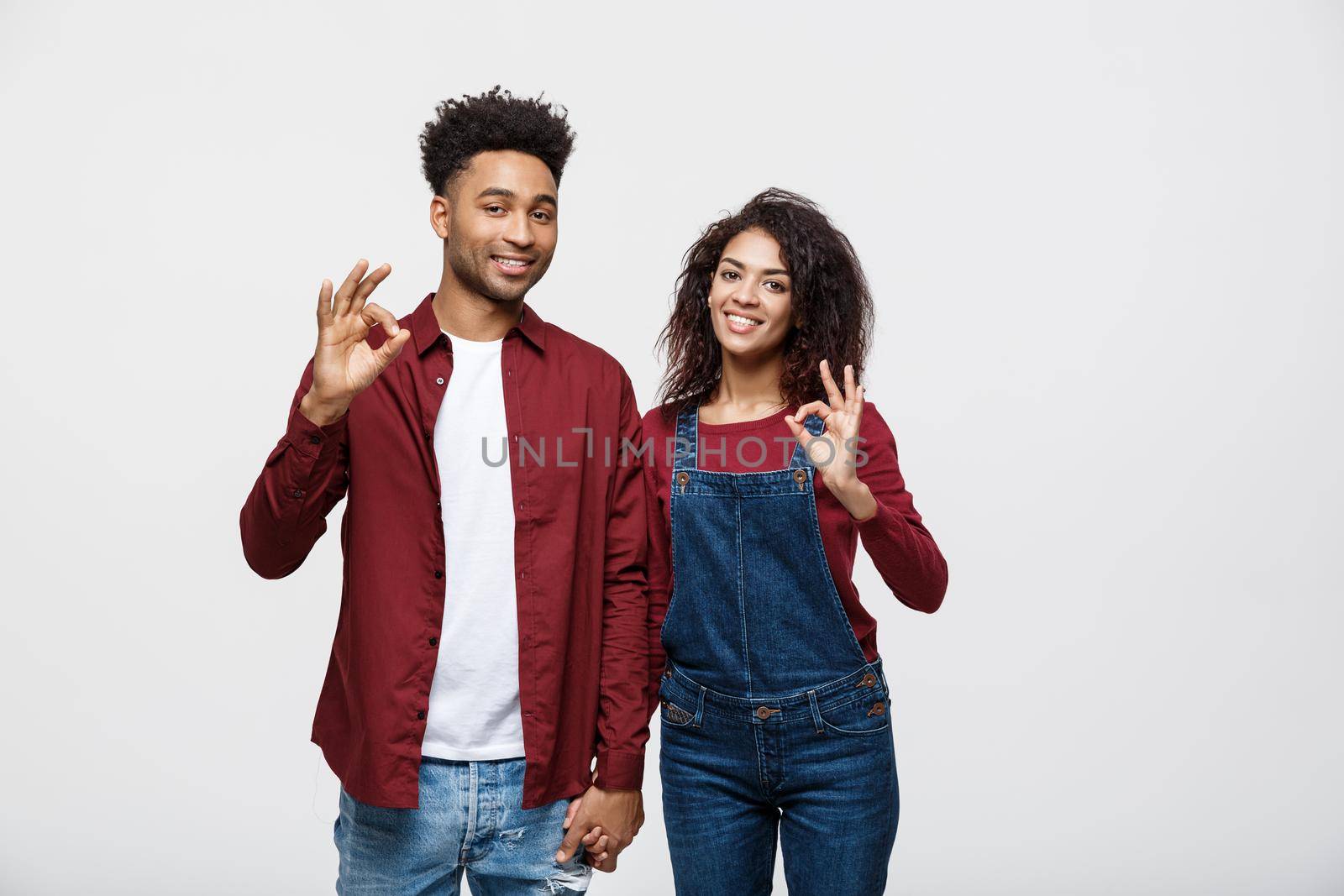 Portrait of a cheerful young african couple standing together and showing ok gesture isolated over white background.