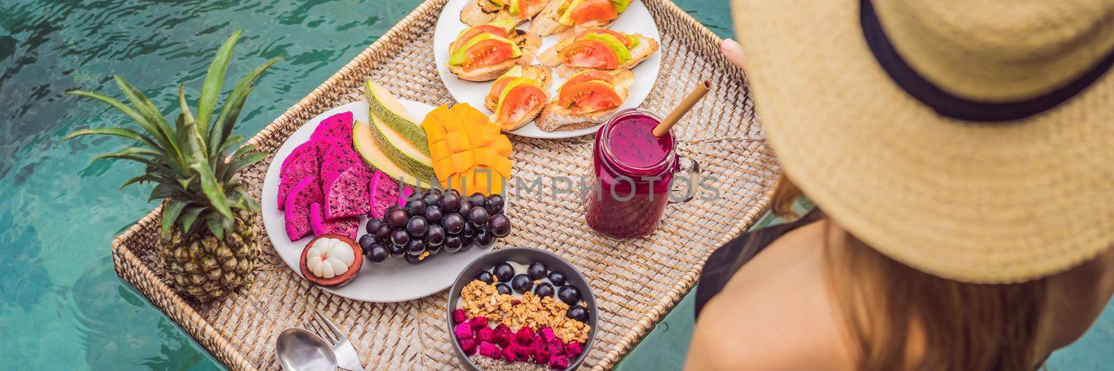 BANNER, LONG FORMAT Breakfast tray in swimming pool, floating breakfast in luxury hotel. Girl relaxing in the pool drinking smoothies and eating fruit plate, smoothie bowl by the hotel pool. Exotic summer diet. Tropical beach lifestyle. Bali Trend by galitskaya