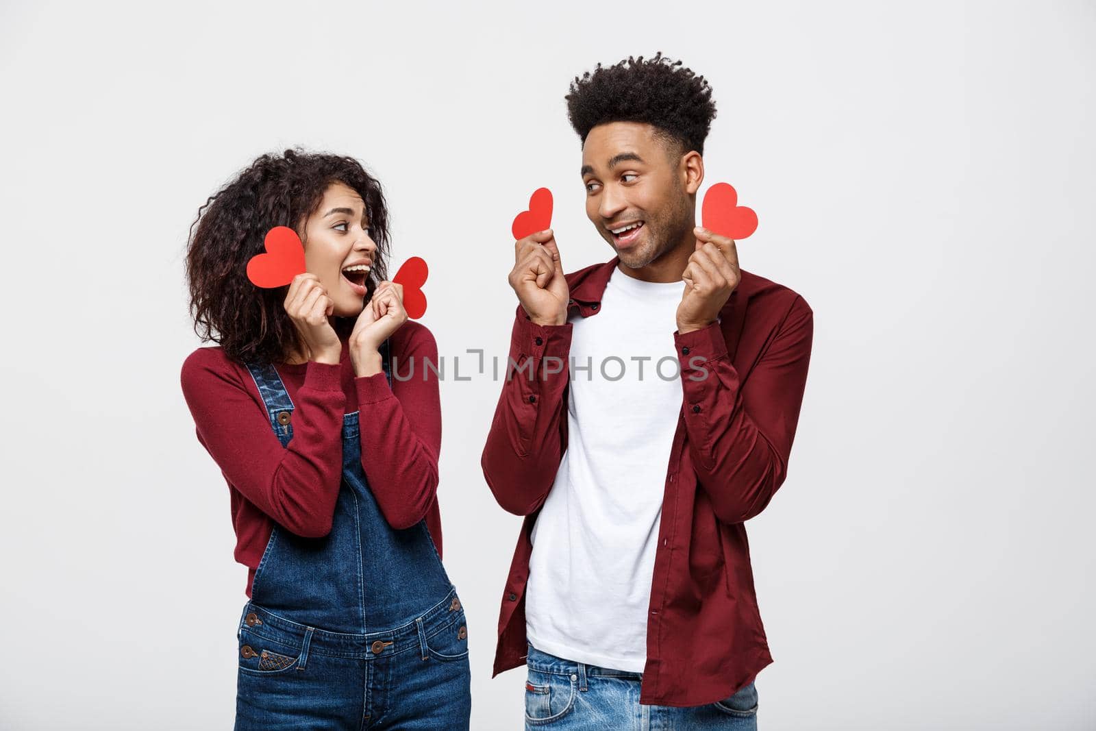 Beautiful Afro American couple holding two red paper heart, looking at camera and smiling, isolated on white background.