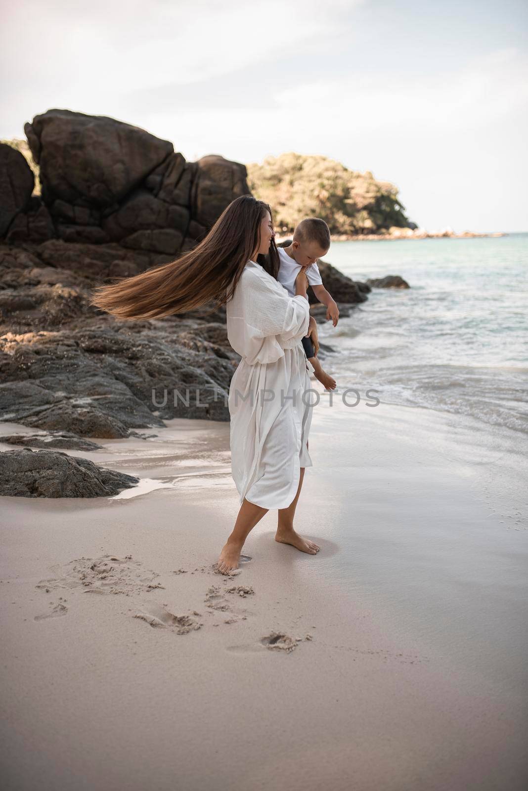 Happy smile european family have rest and run on white sand beach. Father, long black chestnut hair mother, blond baby boy. white cotton clothes. boho dress. t-shorts.Thailand. Aquamarine crystal sea