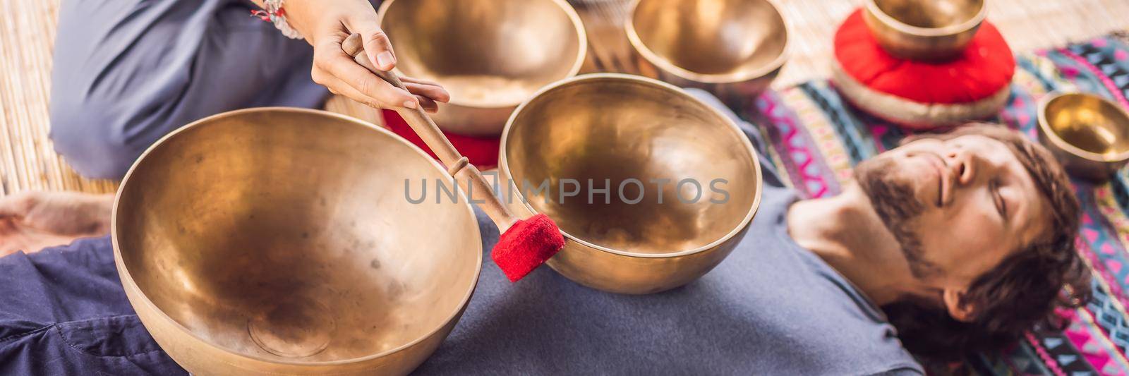 BANNER, LONG FORMAT Nepal Buddha copper singing bowl at spa salon. Young beautiful man doing massage therapy singing bowls in the Spa against a waterfall. Sound therapy, recreation, meditation, healthy lifestyle and body care concept by galitskaya