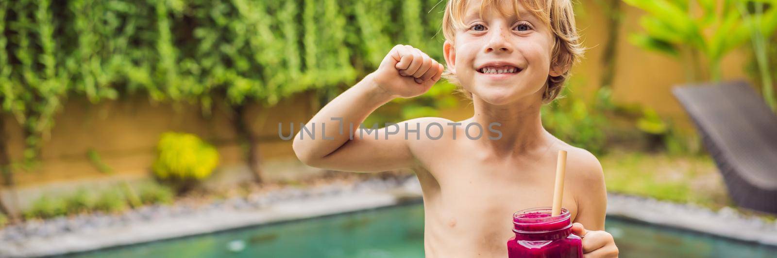 Cute boy holding a bottle of dragon fruit smoothie or juice is flexing his muscles and smiling. BANNER, LONG FORMAT