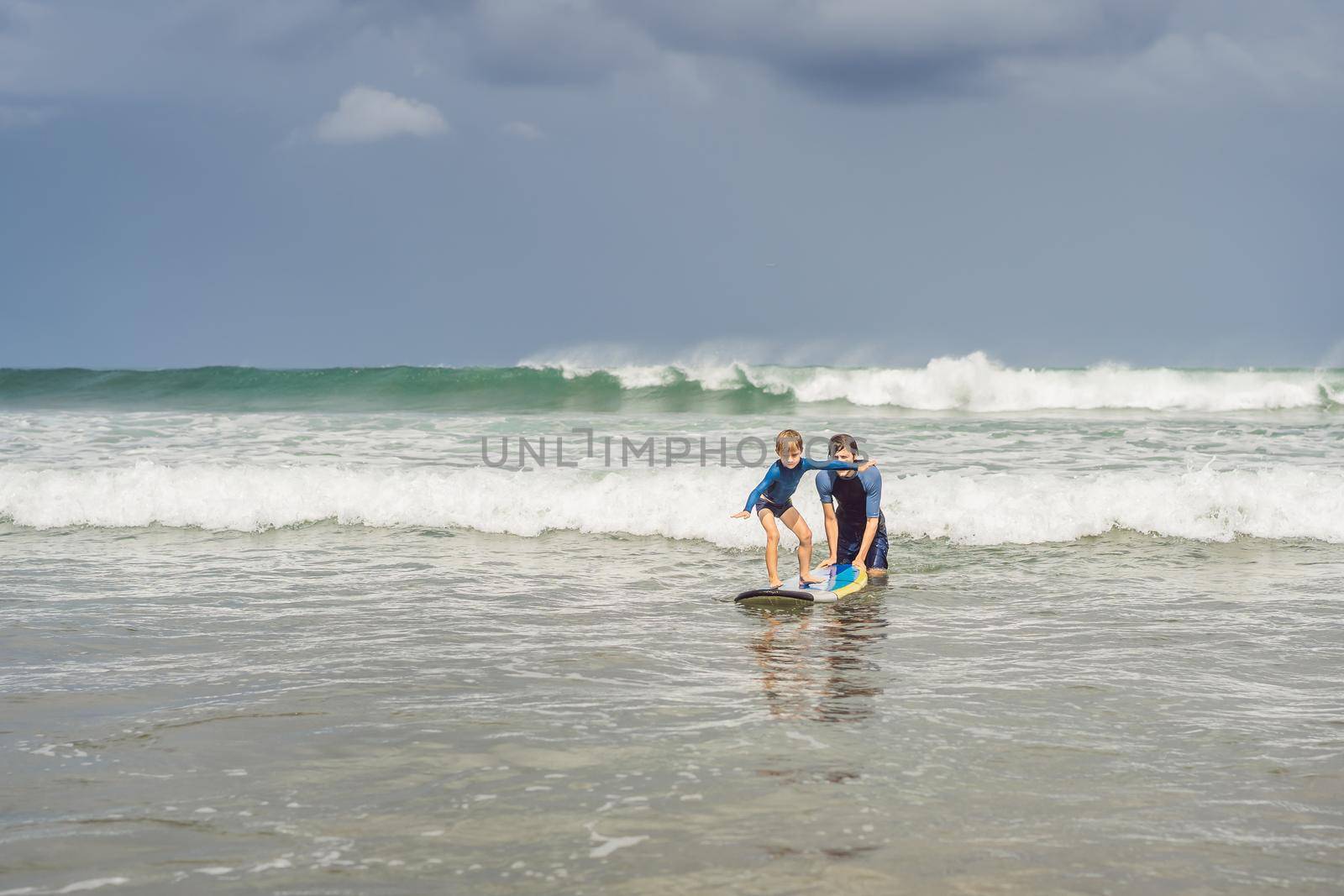 Father or instructor teaching his 5 year old son how to surf in the sea on vacation or holiday. Travel and sports with children concept. Surfing lesson for kids by galitskaya