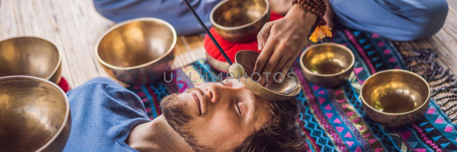 BANNER, LONG FORMAT Nepal Buddha copper singing bowl at spa salon. Young beautiful man doing massage therapy singing bowls in the Spa against a waterfall. Sound therapy, recreation, meditation, healthy lifestyle and body care concept.