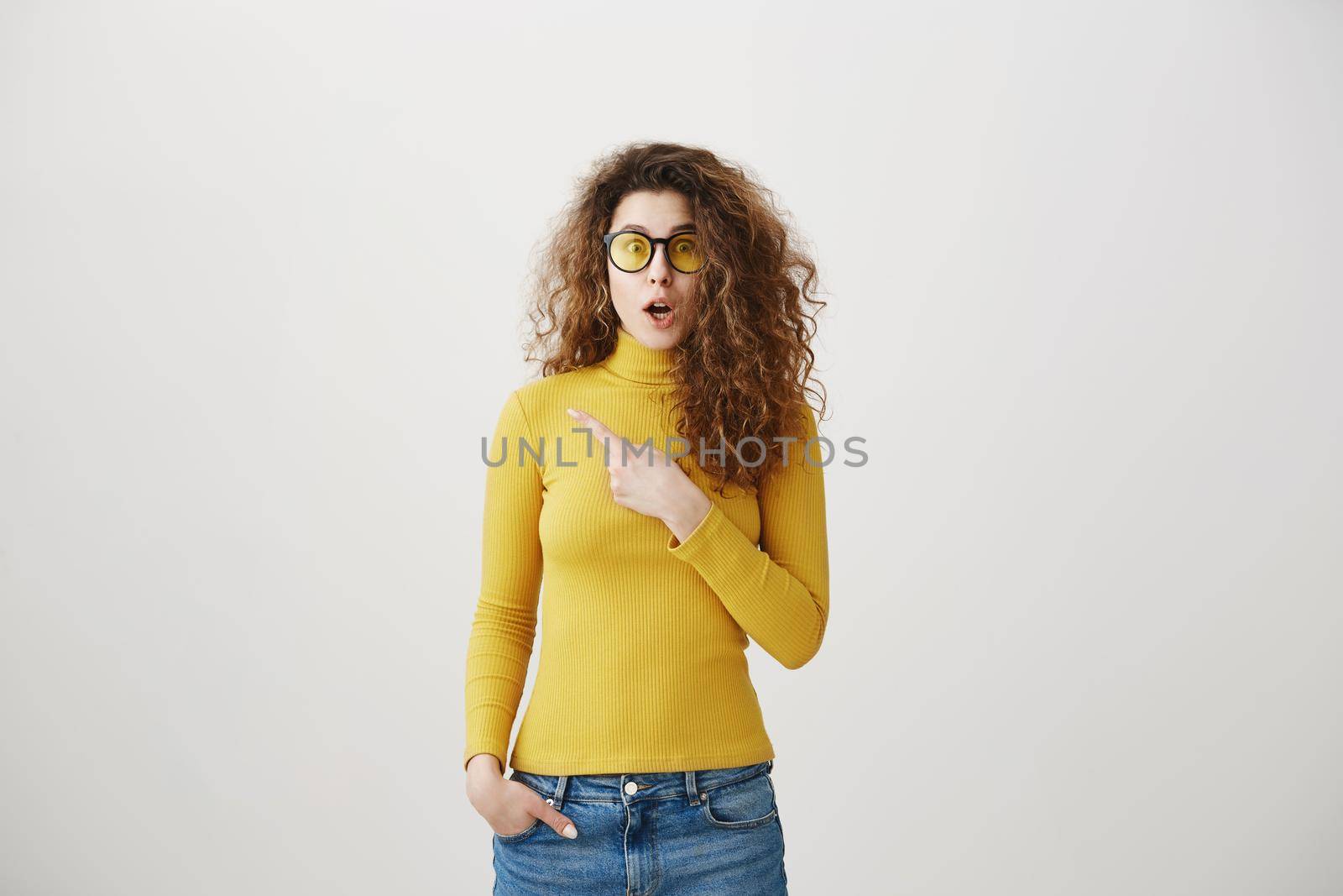 Excited young woman pointing her finger towards blank space isolated over grey background