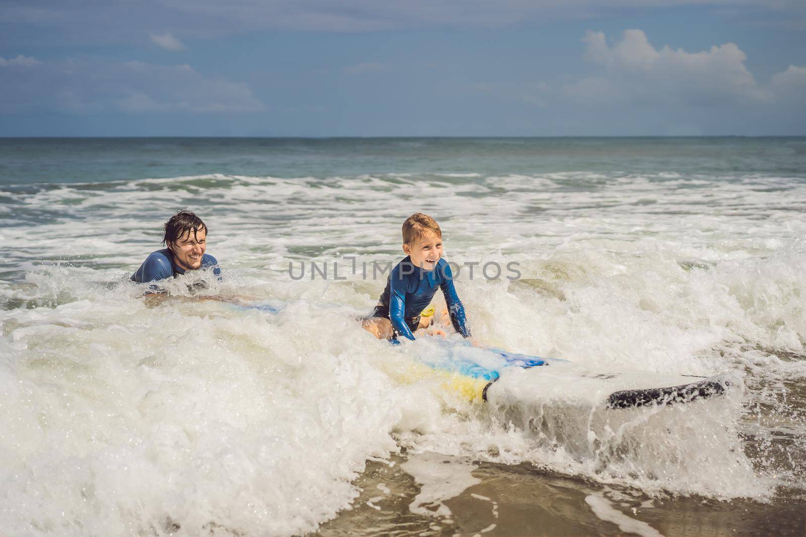 Father or instructor teaching his 5 year old son how to surf in the sea on vacation or holiday. Travel and sports with children concept. Surfing lesson for kids.