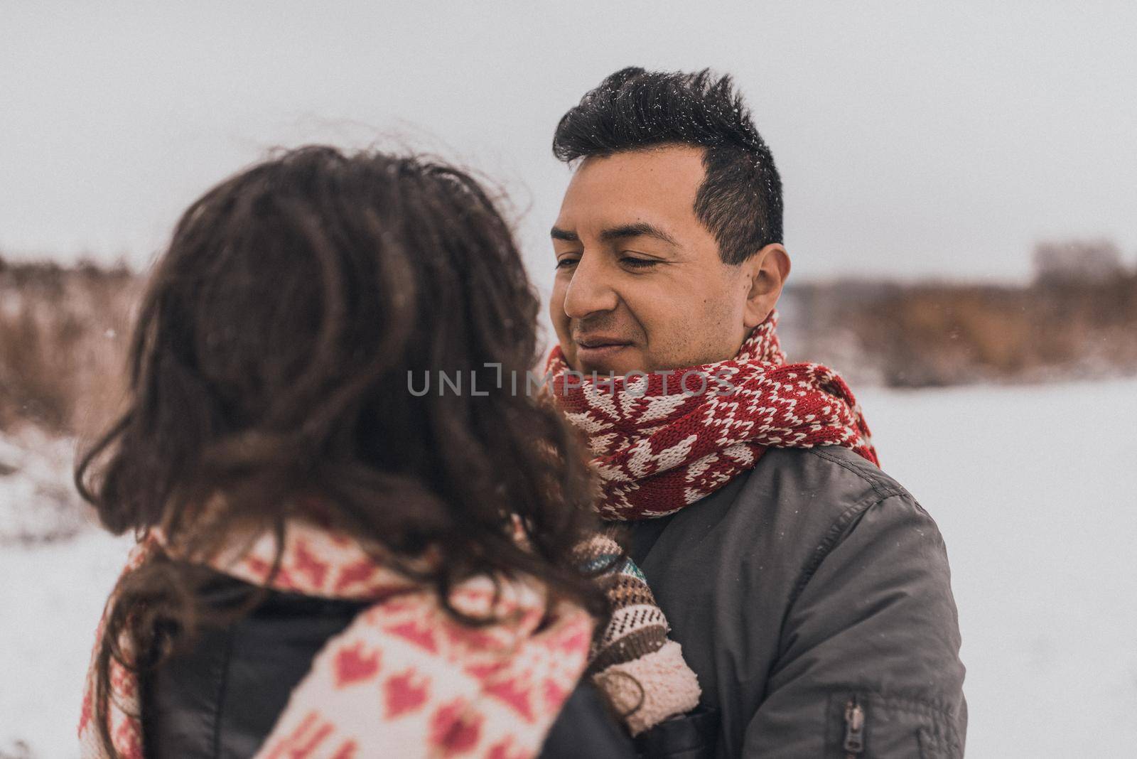 young man and woman stand kissing and hugging. bride and groom in love couple in knitted scarf and mittens in winter with snow and snowflakes. wedding dress. mexican people