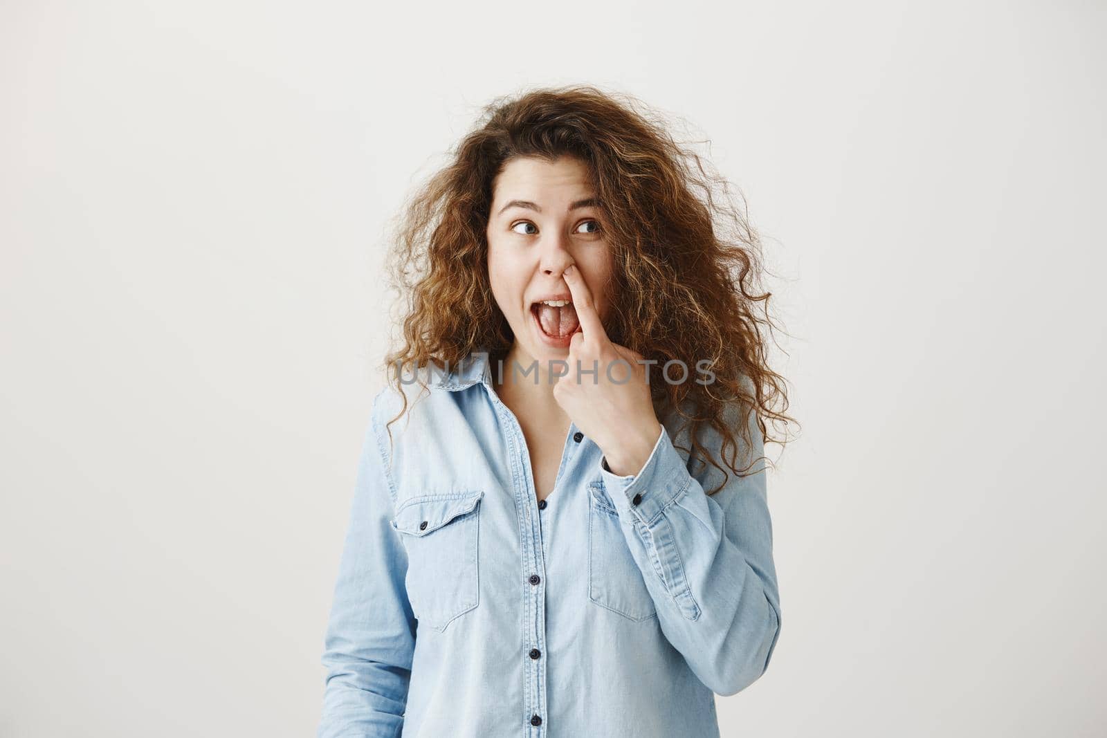 Young girl standing isolated on grey wall playing around looking camera smiling happy close-up.