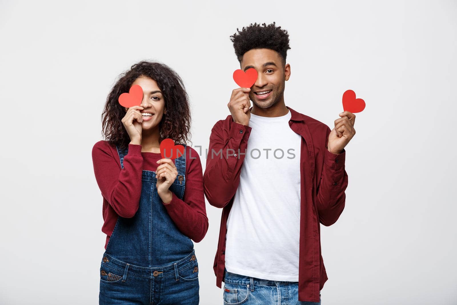 Beautiful Afro American couple holding two red paper heart, looking at camera and smiling, isolated on white background by Benzoix