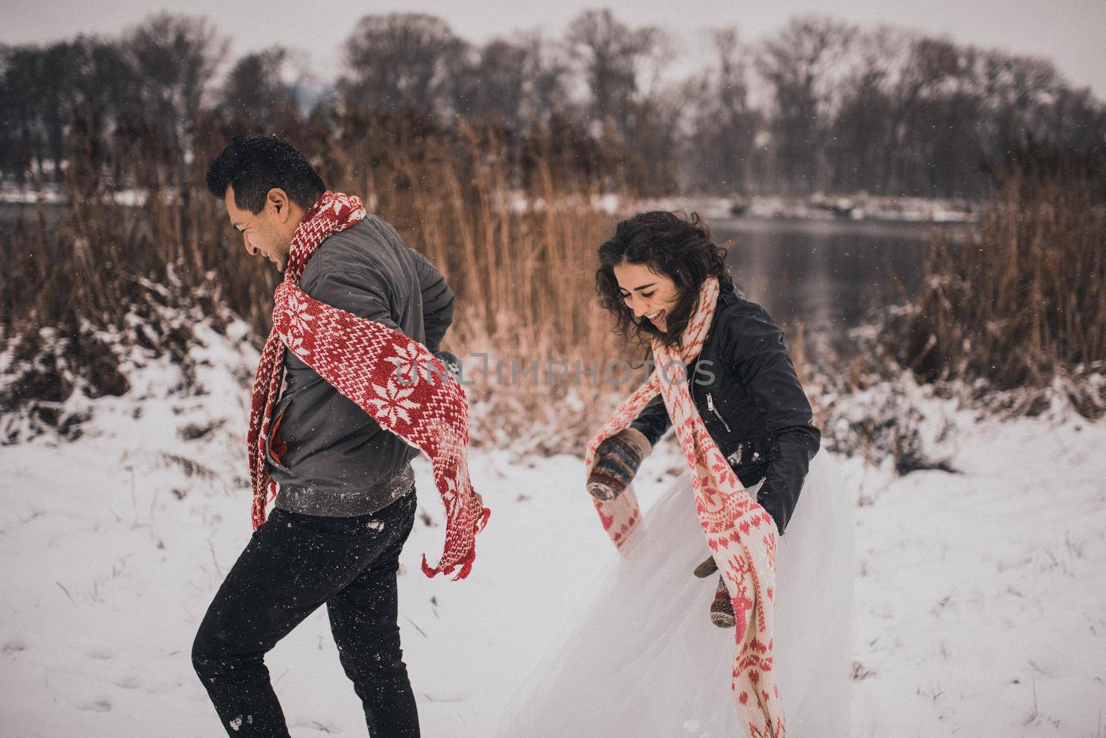 young man and woman running lying in the snow laughing fooling around having fun playing snowballs.bride and groom in love couple in knitted scarf and mittens in winter and snowflakes. mexican people