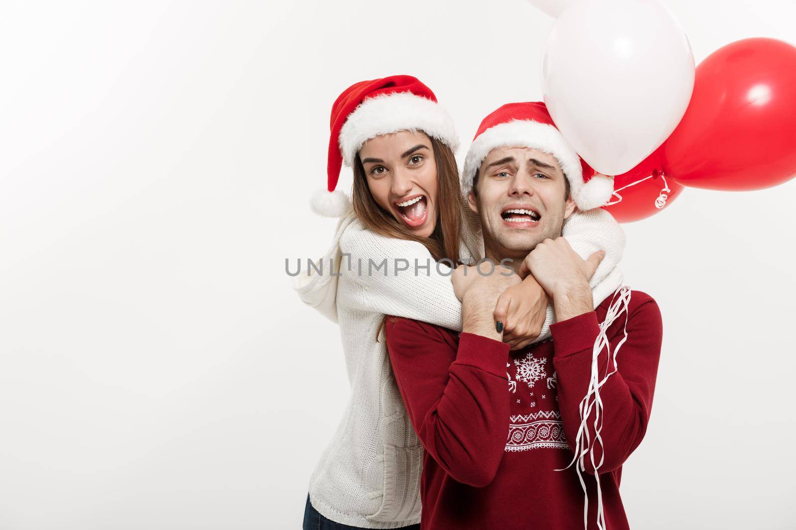 Christmas Concept - Young girlfriend holding balloon is hugging and playing with her boyfriend doing a surprise on Christmas by Benzoix