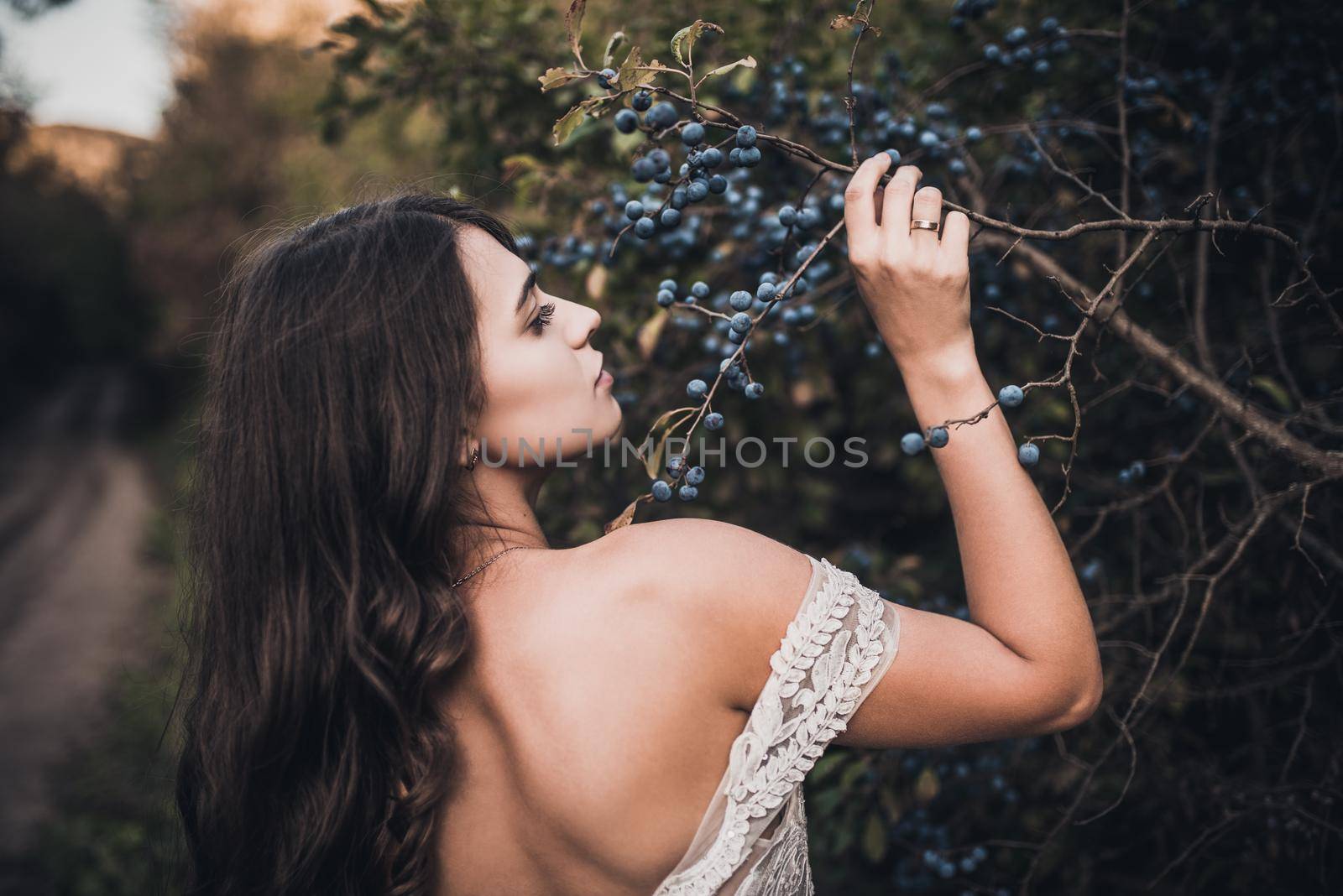 Woman Long-haired bride with bare shoulders near green bush with blueberries in summer