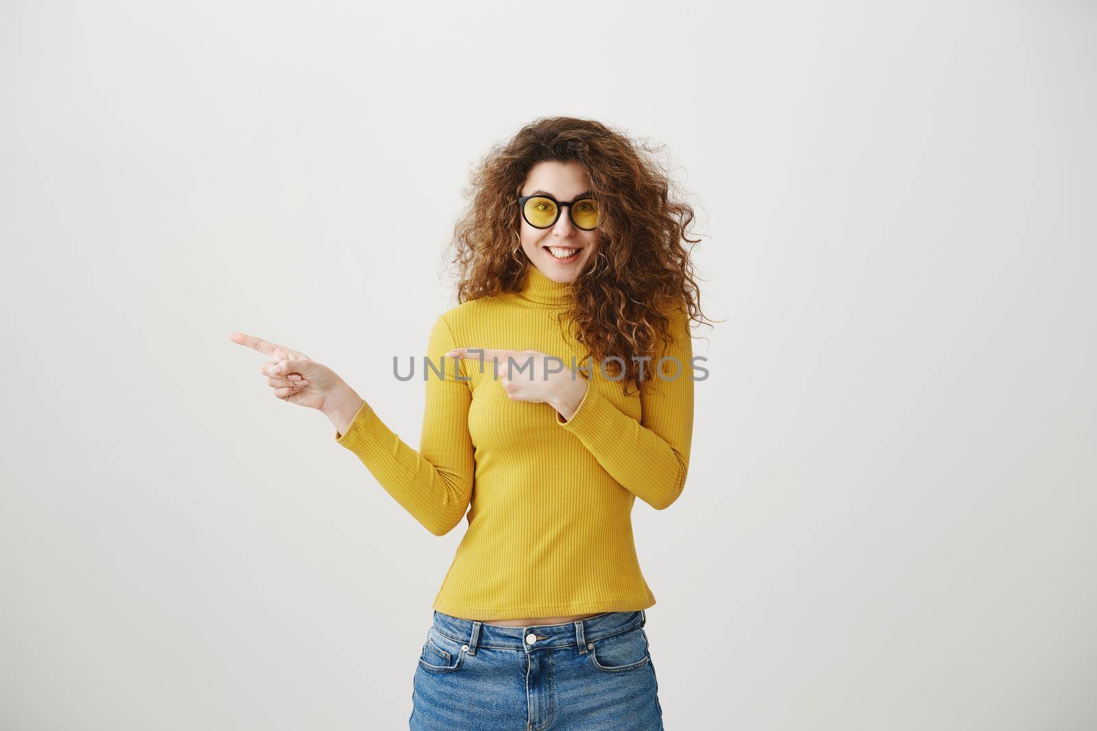 Excited young woman pointing her finger towards blank space isolated over grey background