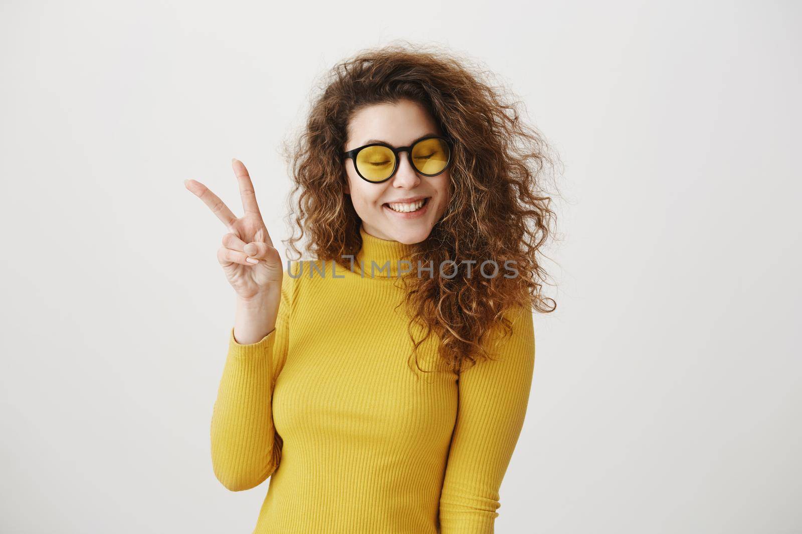 Portrait of cheerful young woman showing two fingers or victory gesture, over grey background
