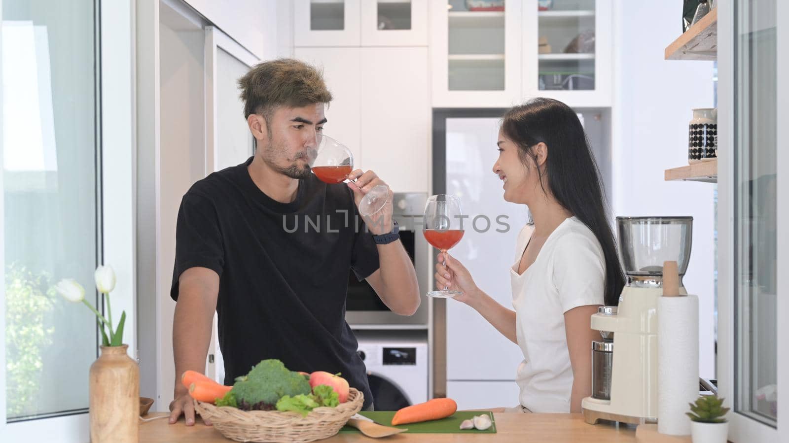 Lovely young couple preparing healthy food and drinking wine at modern home kitchen by prathanchorruangsak