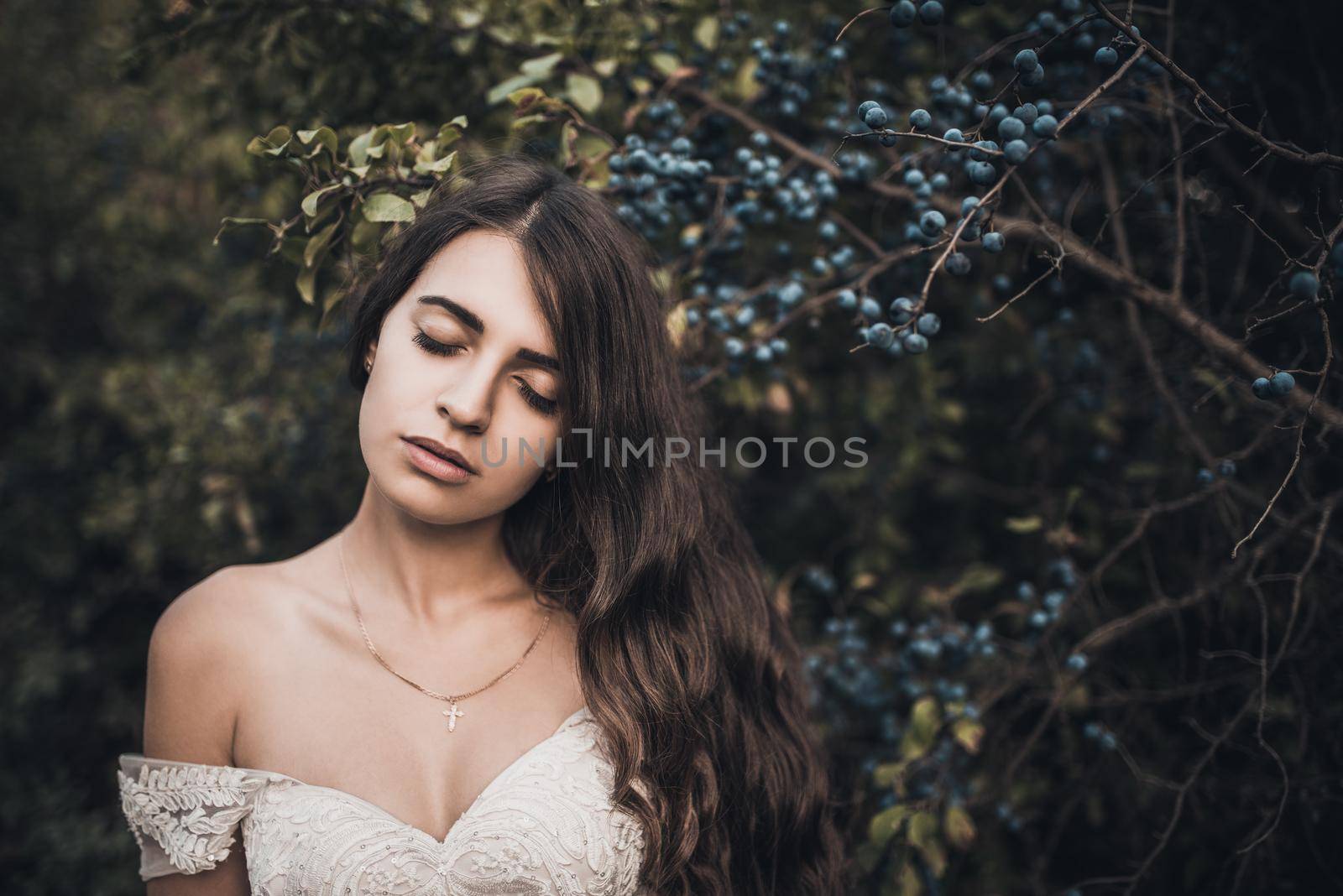 Woman Long-haired bride with bare shoulders near green bush with blueberries in summer