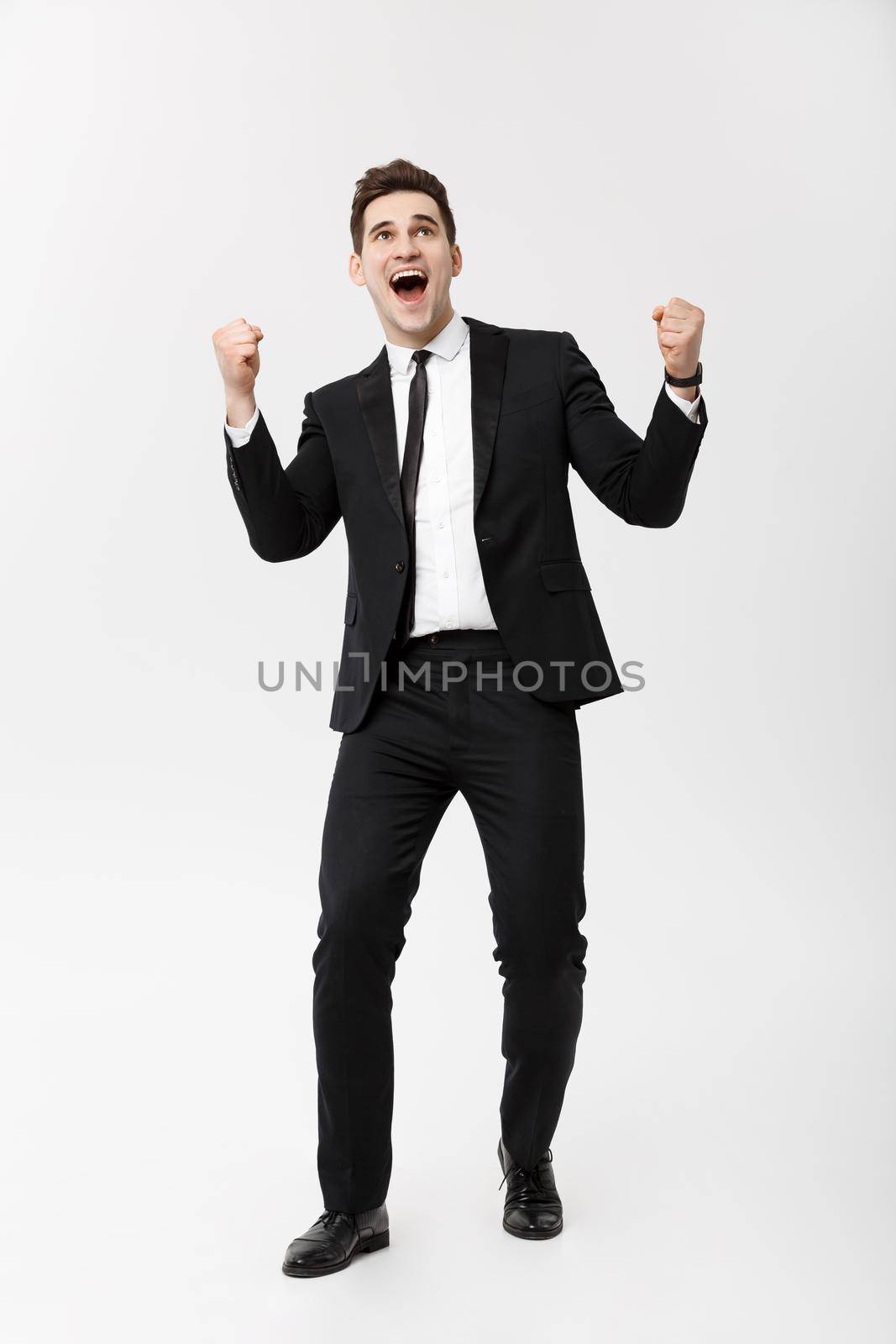 Business Concept: Full-length Portrait excited handsome business man with arms raised in success. Isolated on grey background