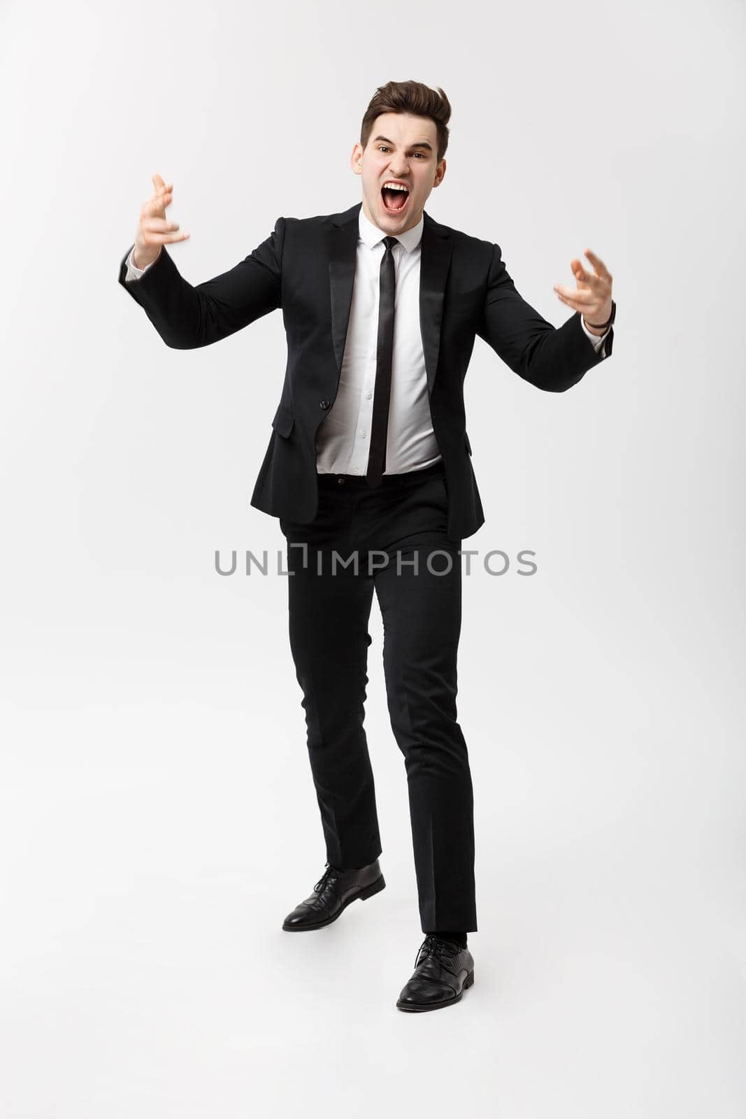 Business Concept: Full-length Portrait of a mad businessman in suit yelling and screaming while standing over isolated gray background