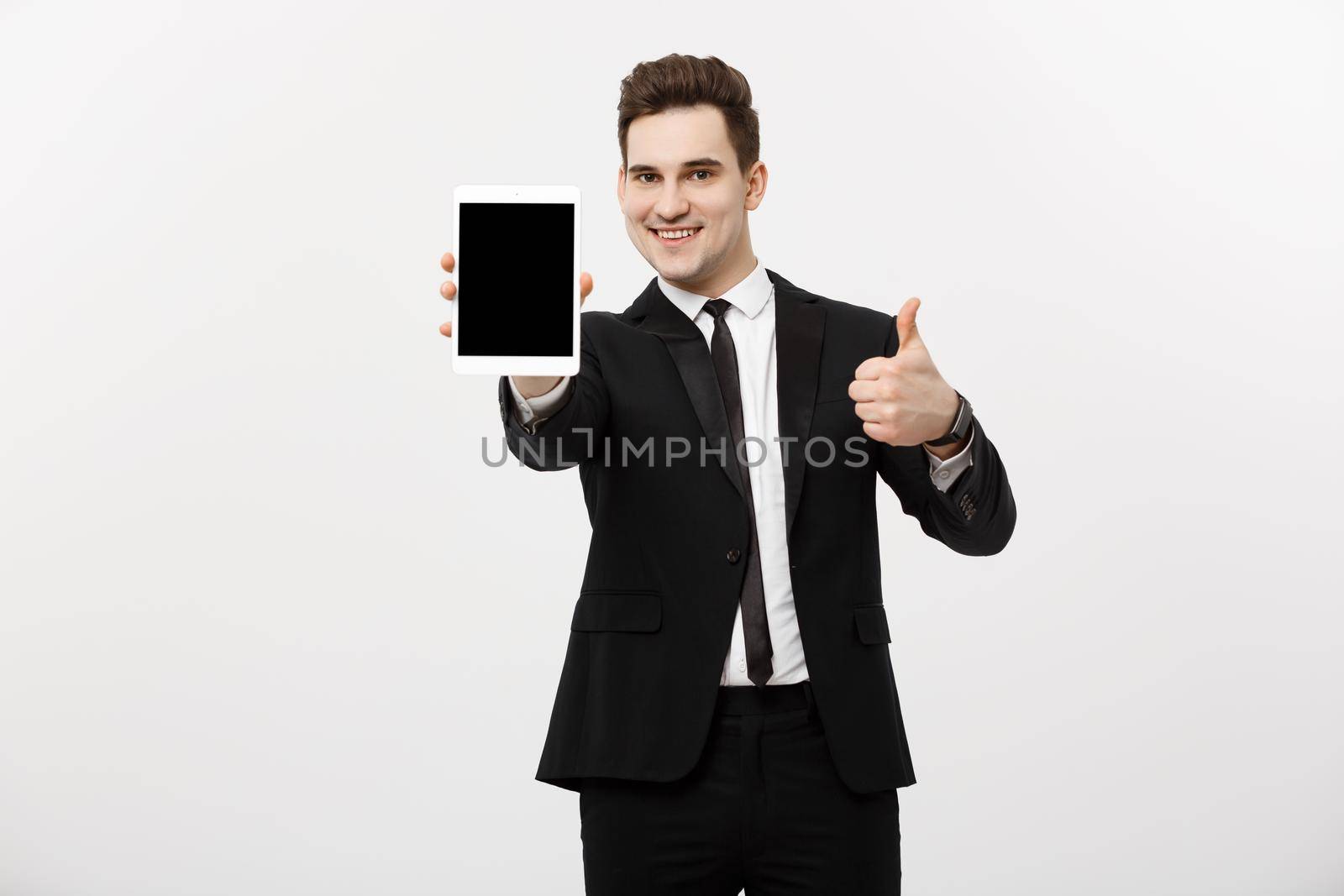 Business Concept: smiling businessman with tablet showing thumbs up over gray studio background.