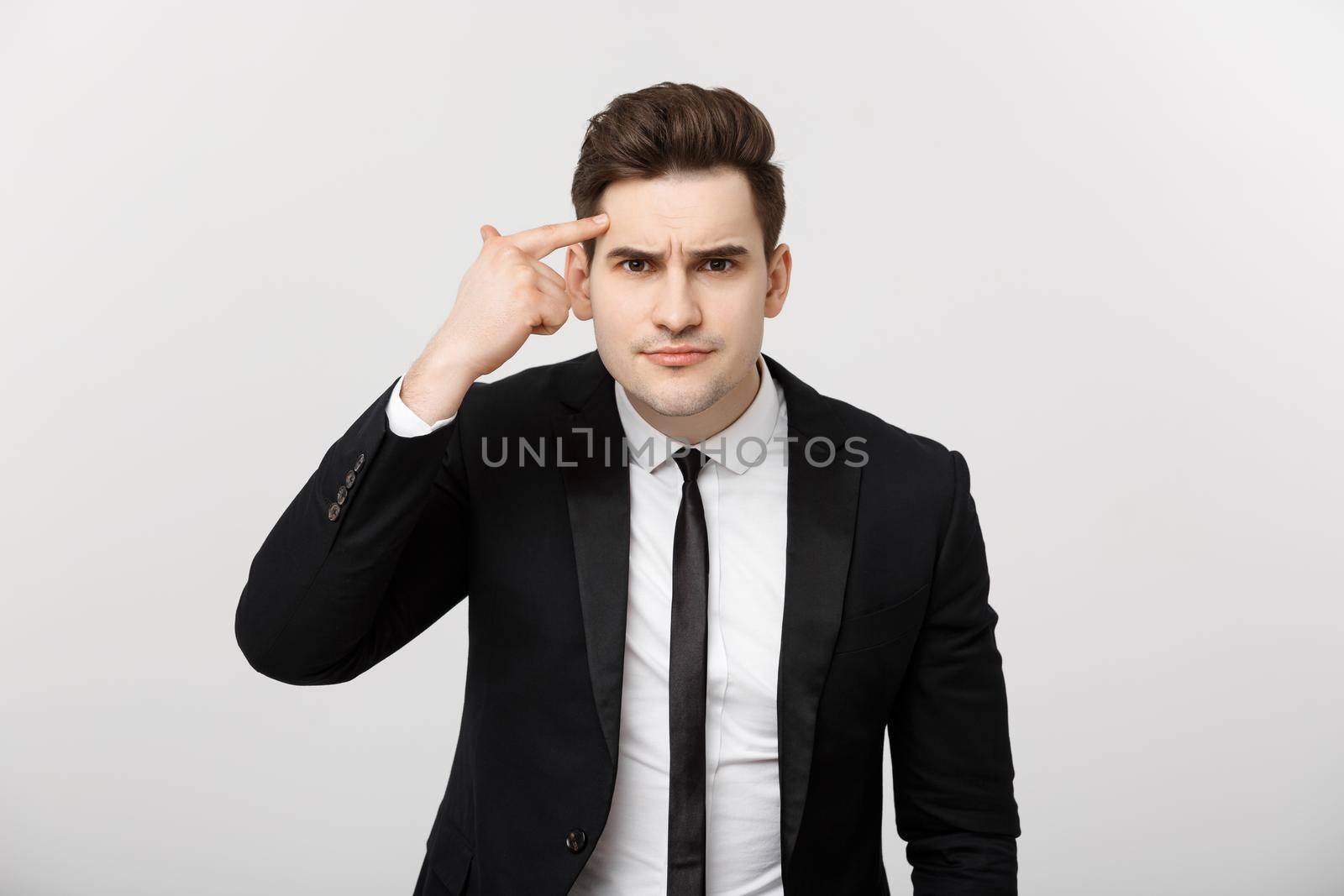 Business man points his finger at his head and thinking isolated on a gray background.