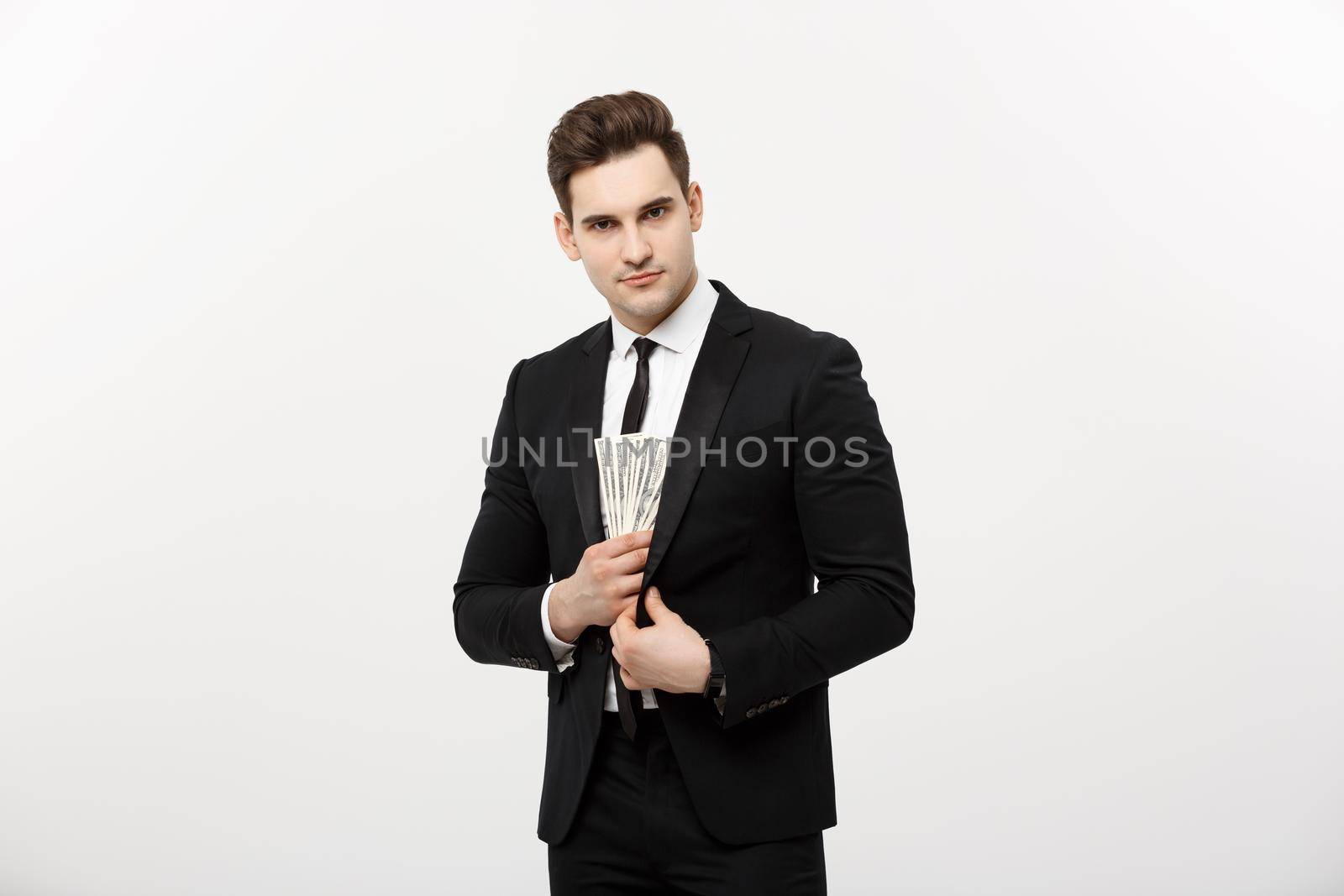 Business Concept: Handsome businessman in black suit taking dollars banknotes with stealthy expression against white background
