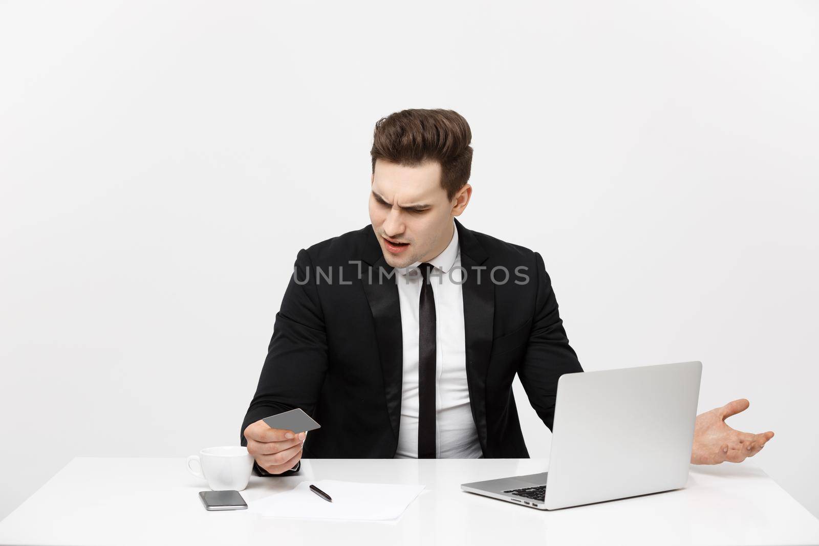 Business Concept: Portrait of young businessman using laptop computer and mobile phone holding debit card. Isolated over grey background