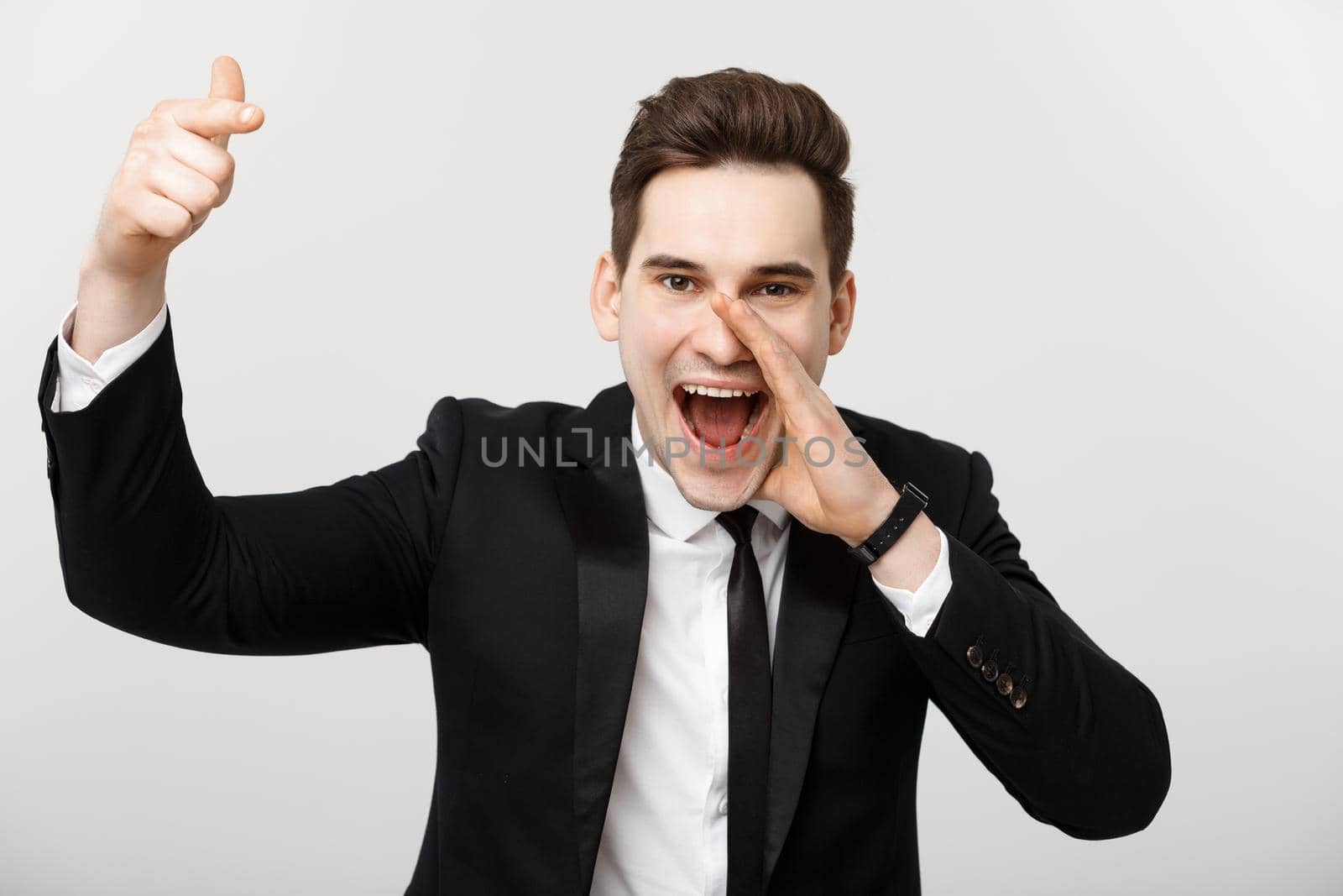 Portrait of a happy businessman in suit pointing finger away over isolated grey background.
